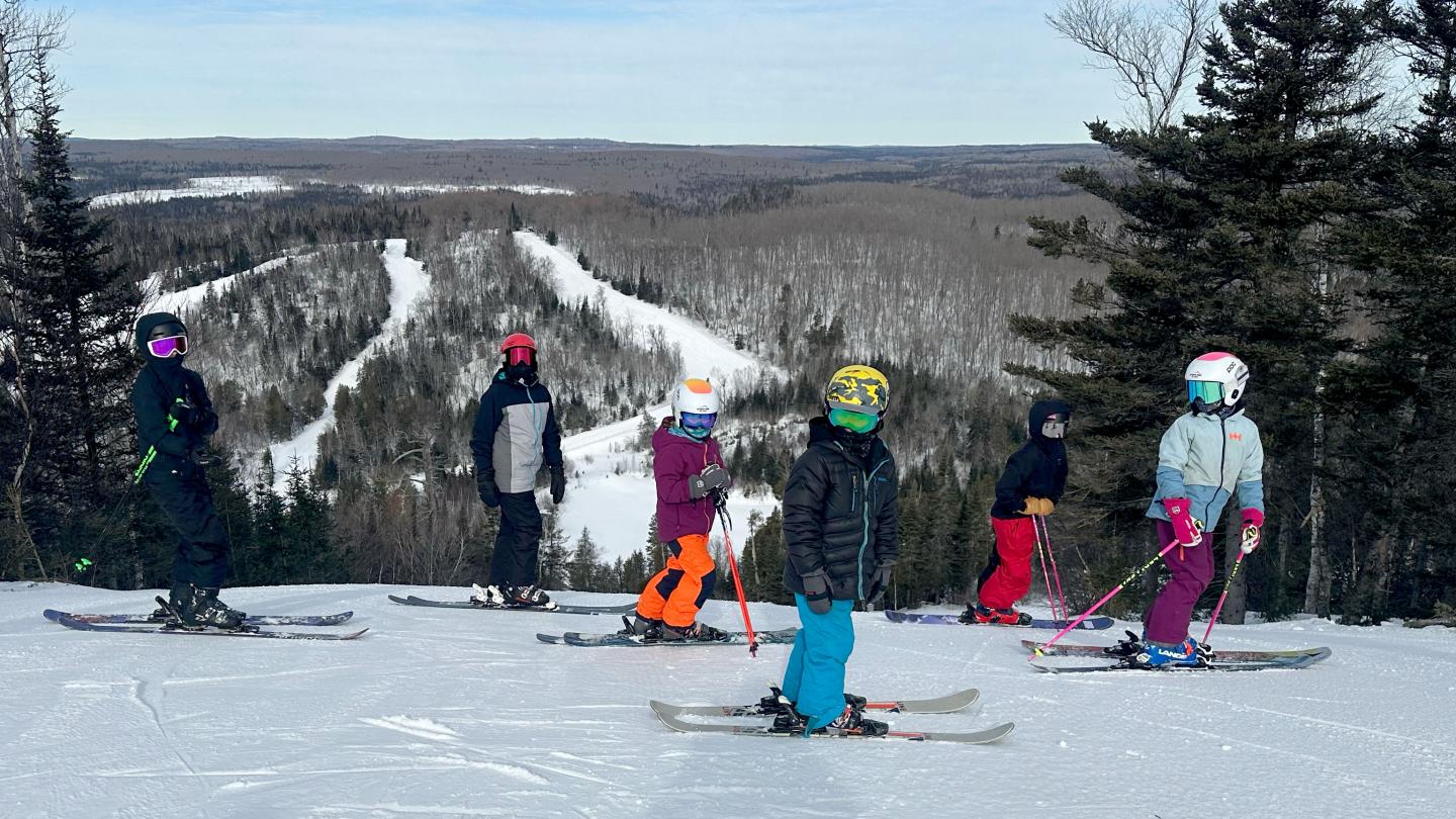 Skiers on a snowy slope with a forested valley backdrop.