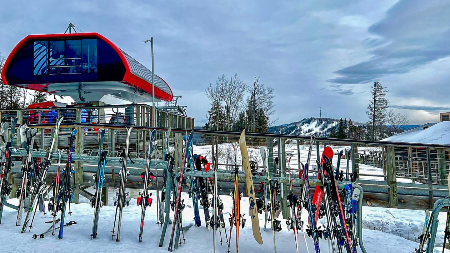 Ski racks with skis at snowy mountain resort under cloudy sky.