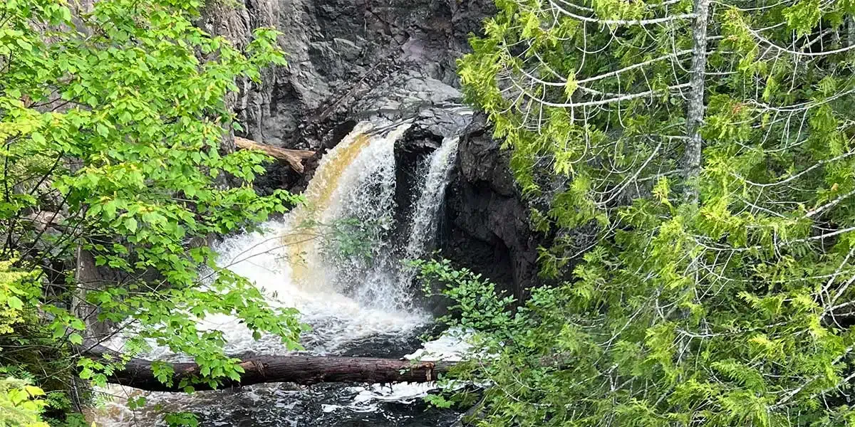 Waterfall surrounded by lush green trees and rocks.