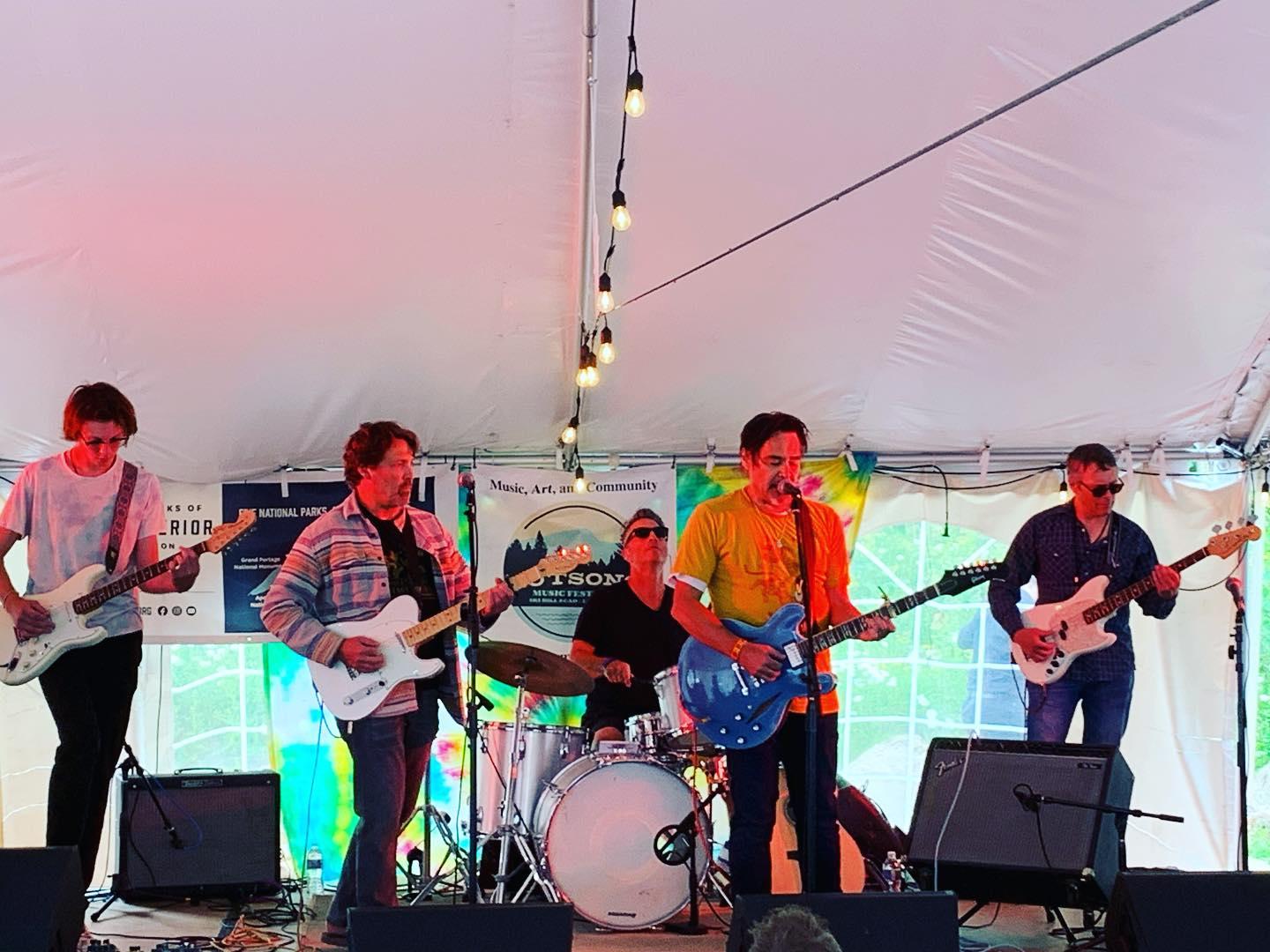 Band playing under a white tent with colorful lighting.