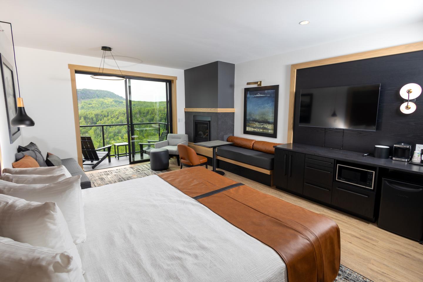 Modern hotel room with a bed, seating area, and balcony view of greenery.