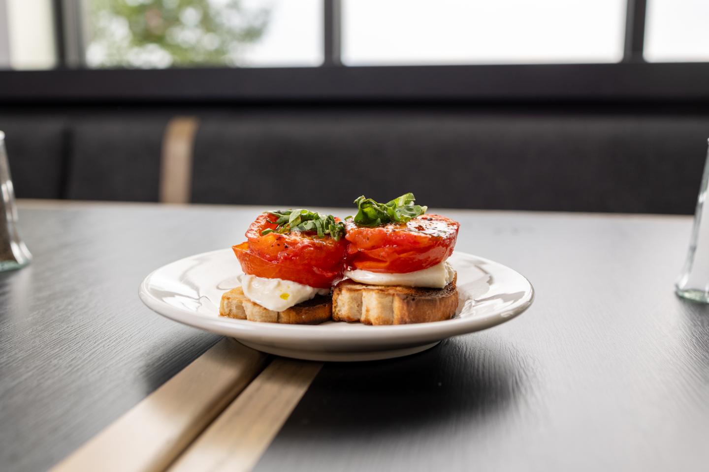 Tomato and mozzarella bruschetta on a white plate in a restaurant setting.