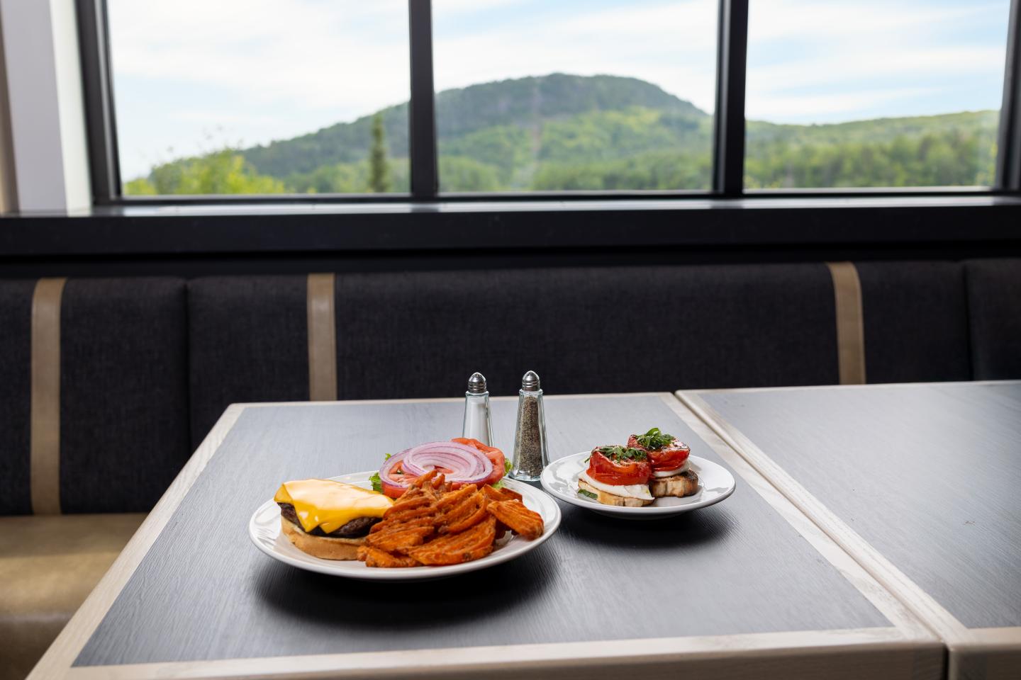 Burger and fries on table by window with mountain view.