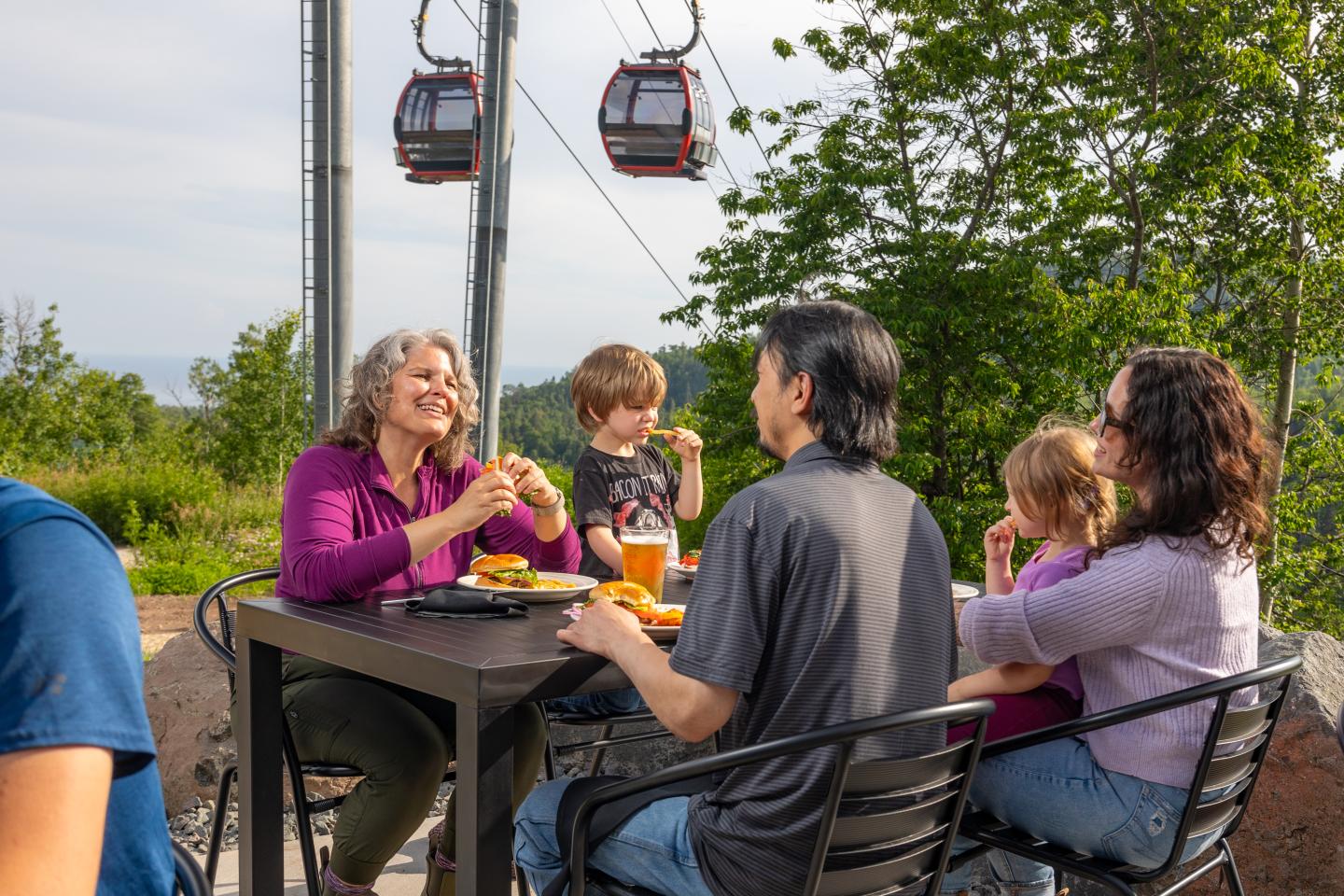 Family dining outdoors near a cable car, surrounded by greenery.