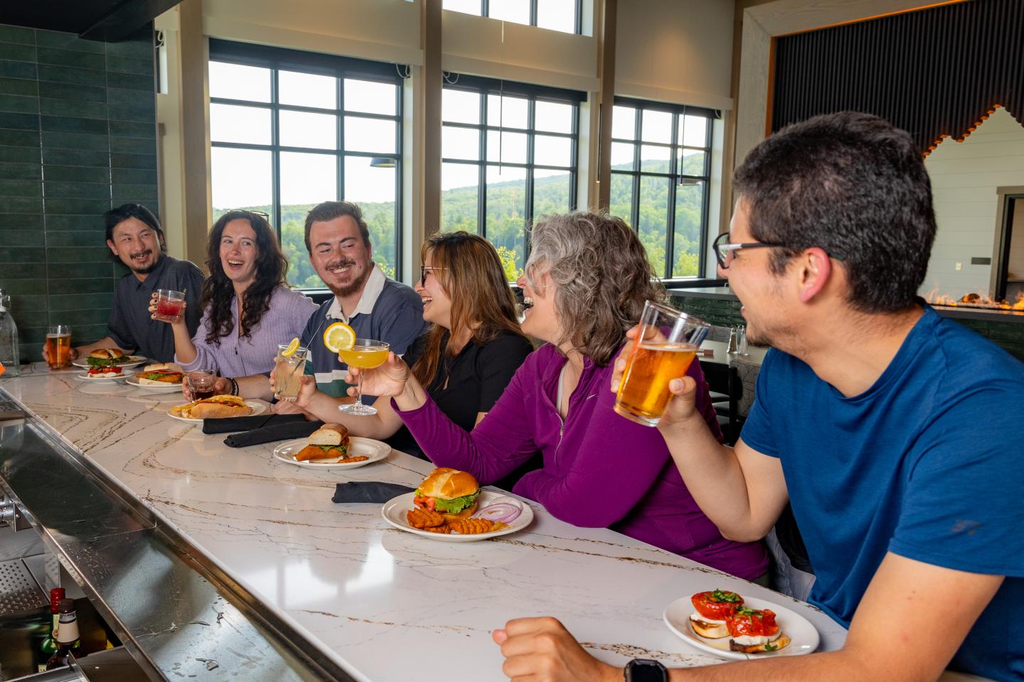 Friends laughing and dining at a bar, holding drinks and burgers.