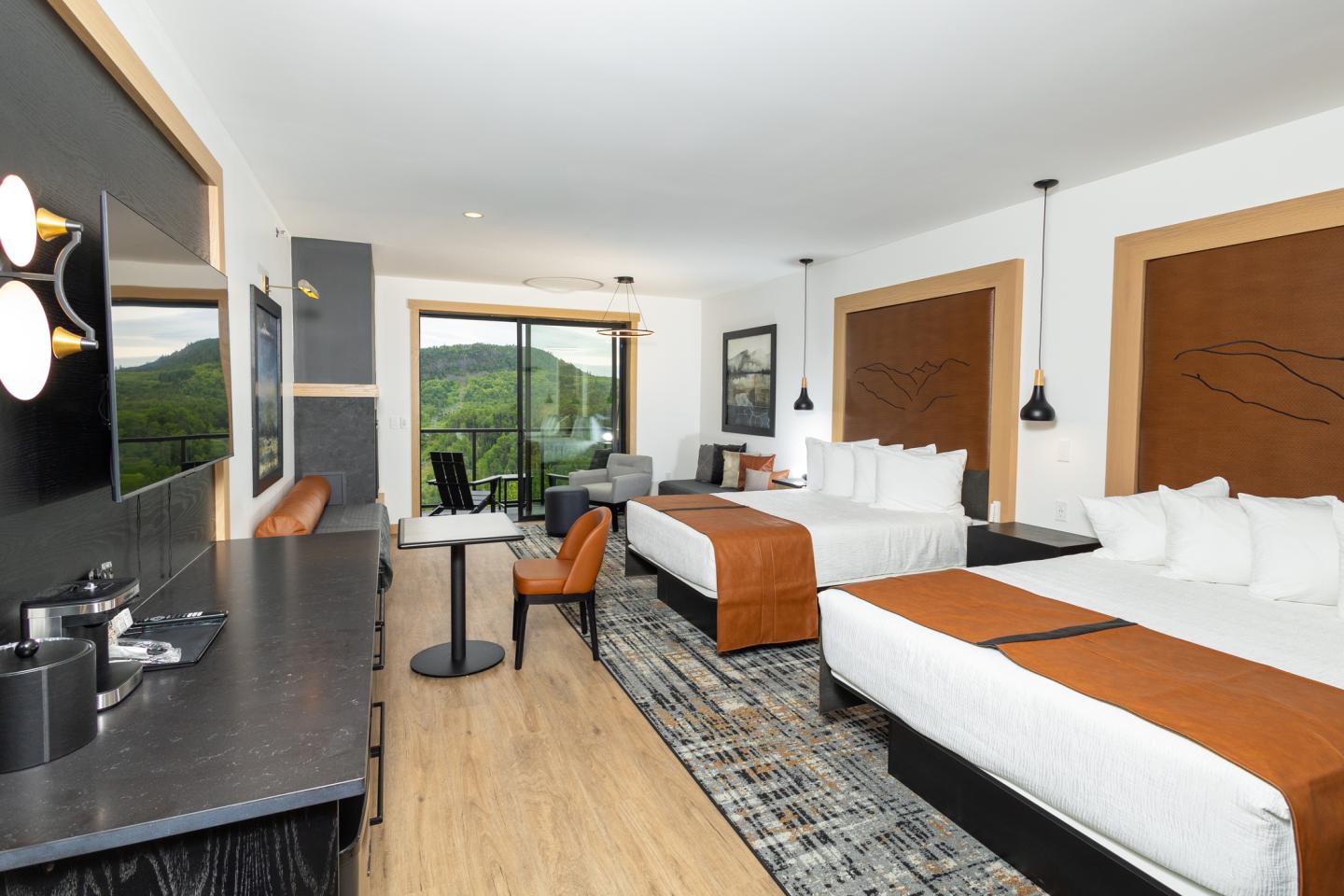 Hotel room with two beds, modern decor, TV, and balcony view of greenery.