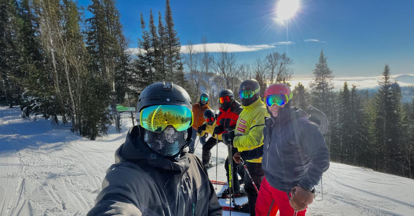 Group of skiers posing on a snowy slope, sunny day with trees in the background.