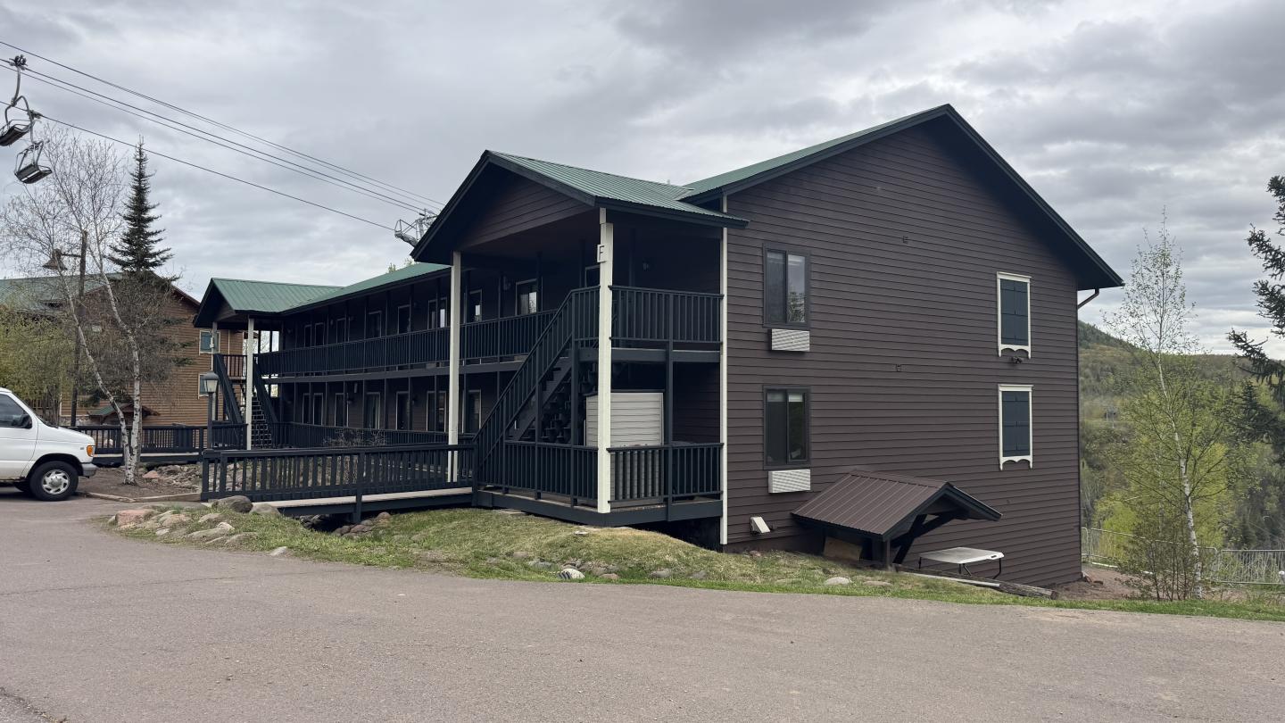 Two-story brown building with green roofs under a cloudy sky.