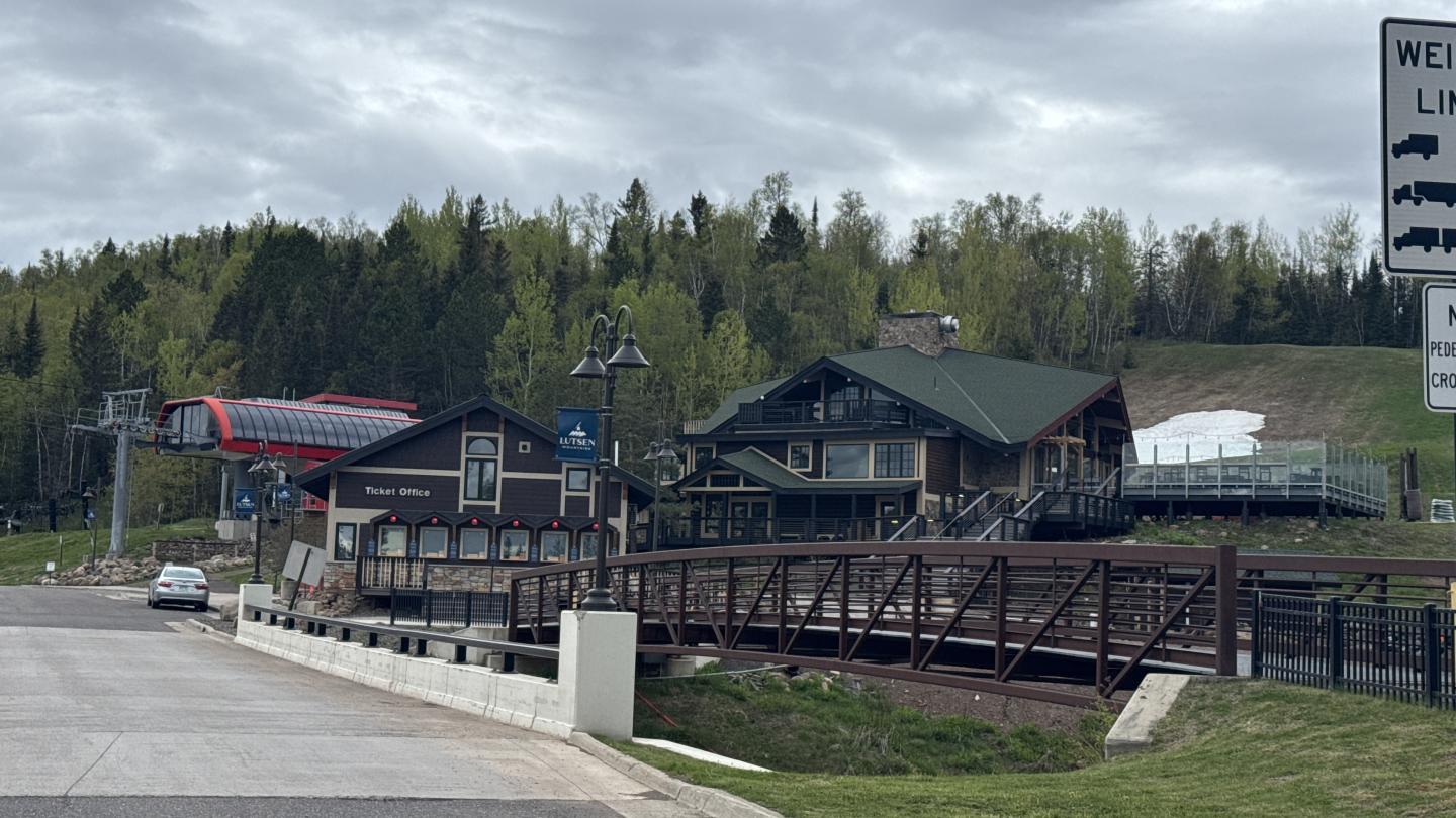 Mountain lodge with green roof, surrounded by trees and overcast sky.
