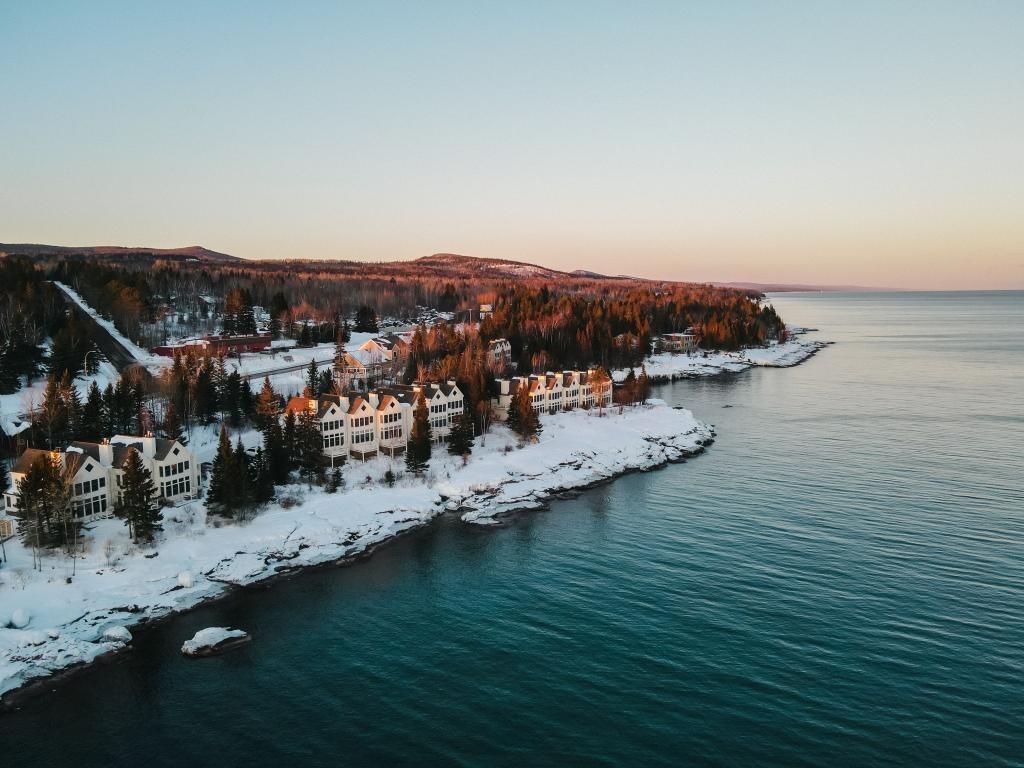Snow-covered coastline at sunset with houses and forests.