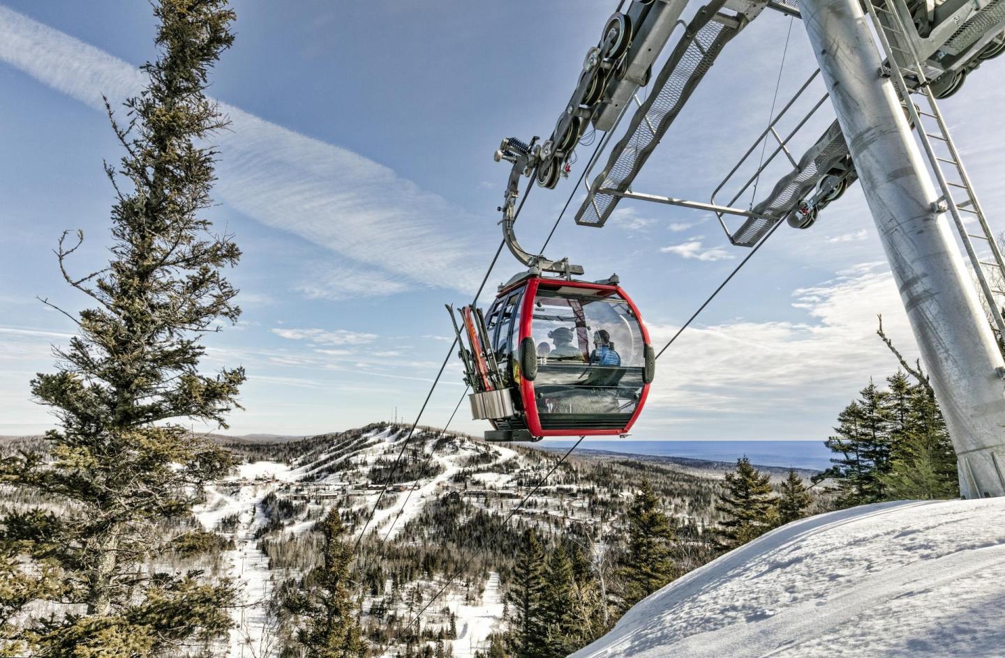 Red gondola over snowy mountain landscape with trees.