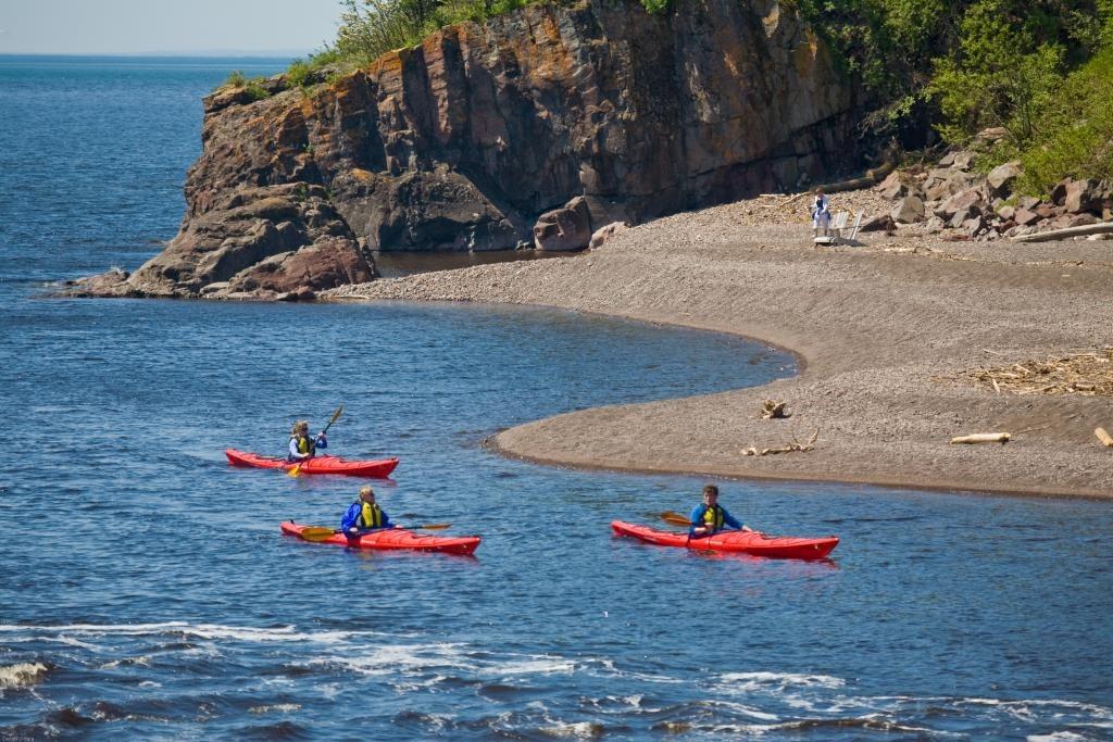Three people kayaking on a calm sea near a rocky shoreline.