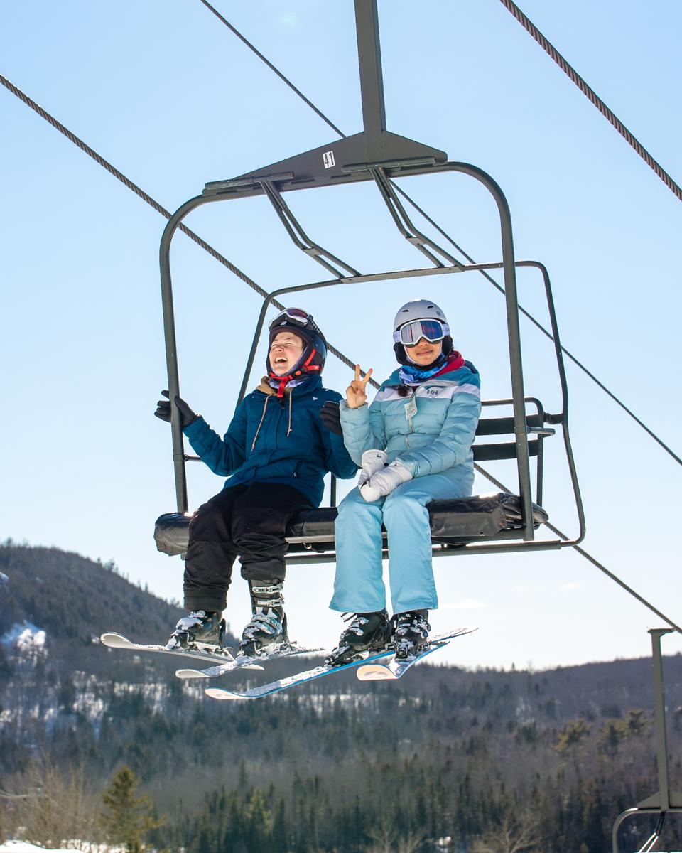 Two skiers riding a chairlift over a snowy mountain landscape.