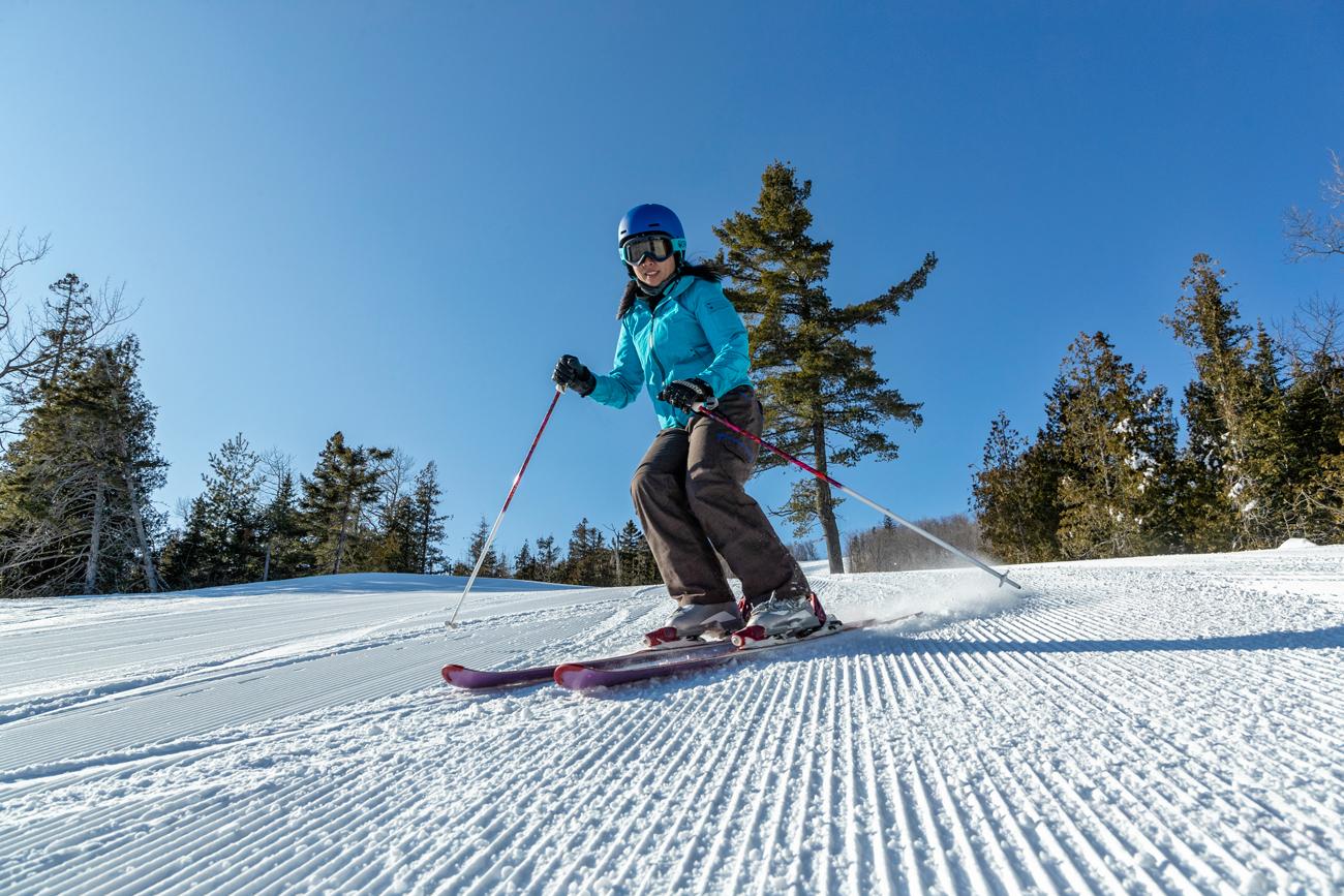 Skier in blue jacket descending a snowy slope under clear blue sky.