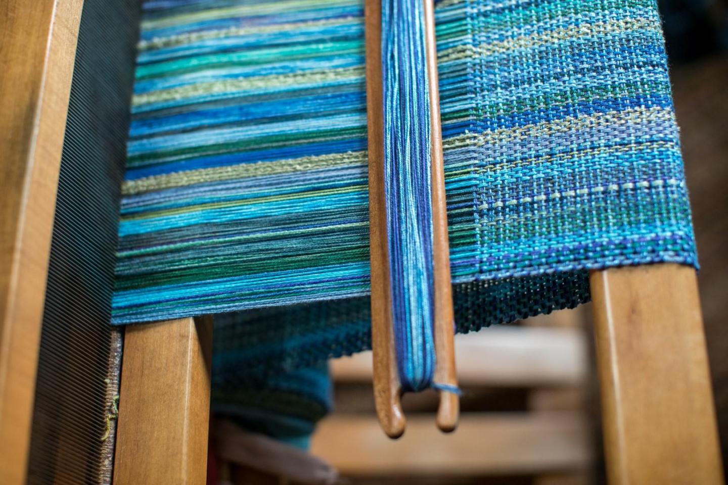 Blue and green woven fabric on a loom with wooden frame.