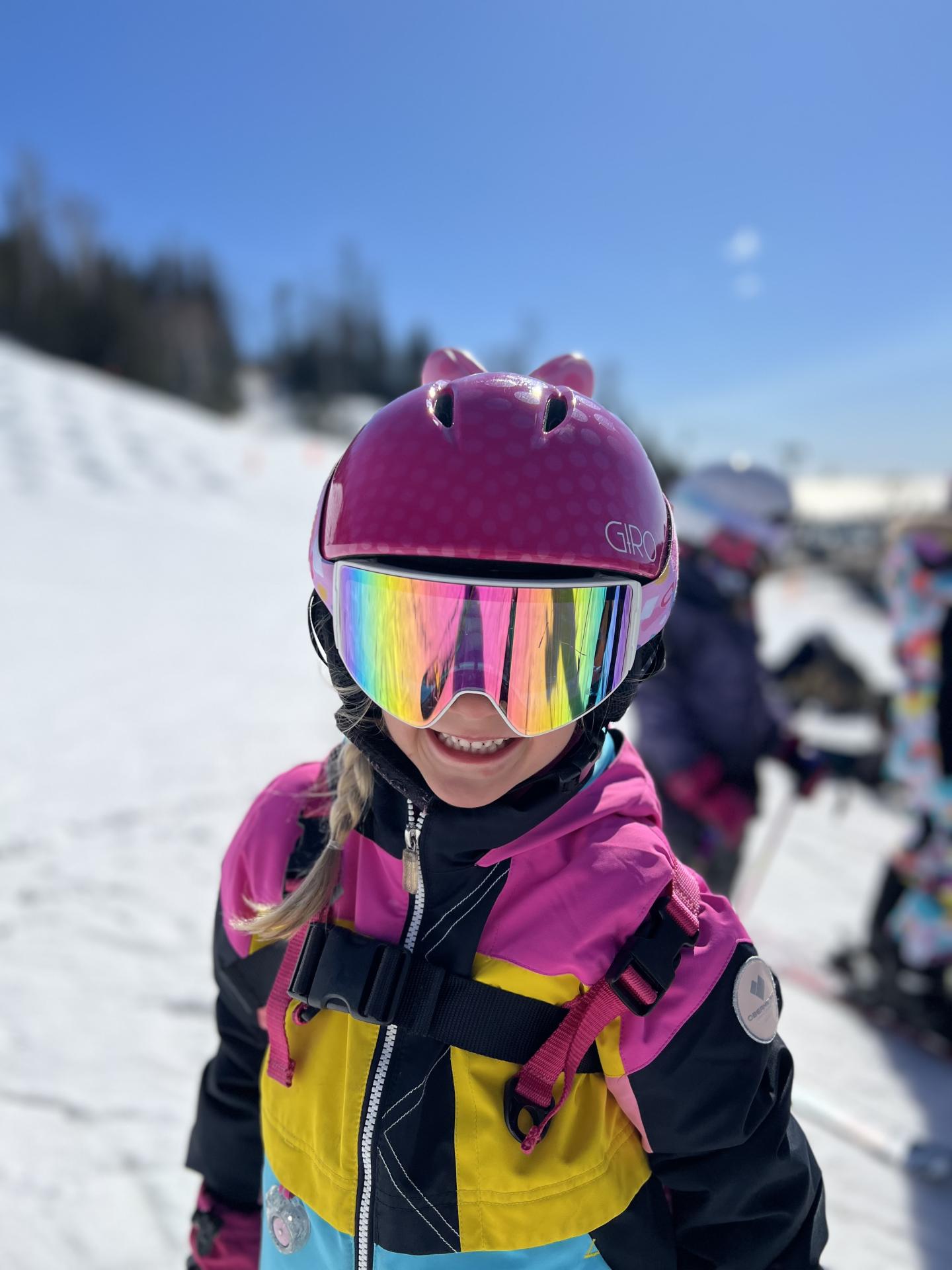 Child in colorful ski gear, smiling on a snowy slope.