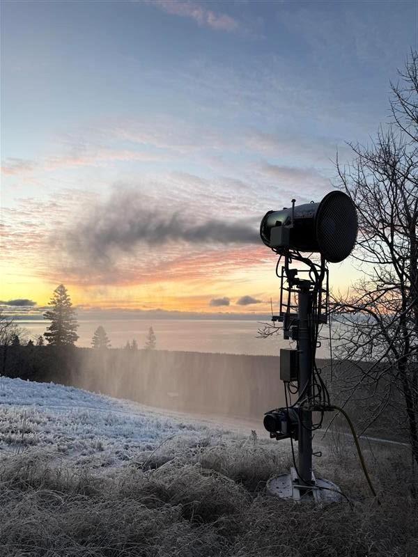Snow machine blowing snow at sunrise with trees and sky in the background.