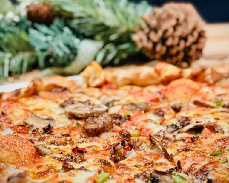 Pizza topped with mushrooms and sausage, pine branches and a cone in the background.
