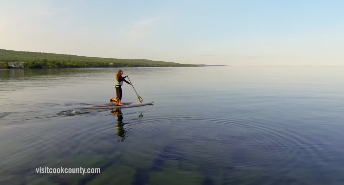 Person paddleboarding on calm lake under clear sky.