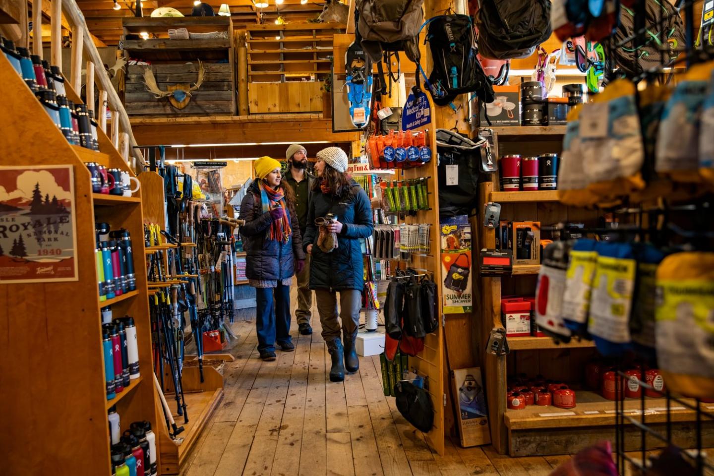 Cozy outdoor gear store with people browsing, wooden floors, colorful merchandise.