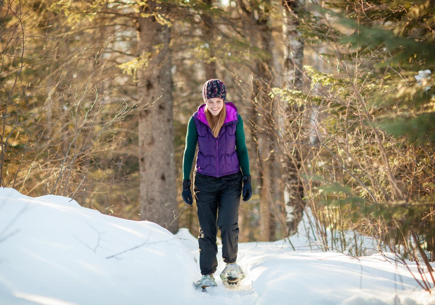 Person snowshoeing through a snowy forest in winter attire.