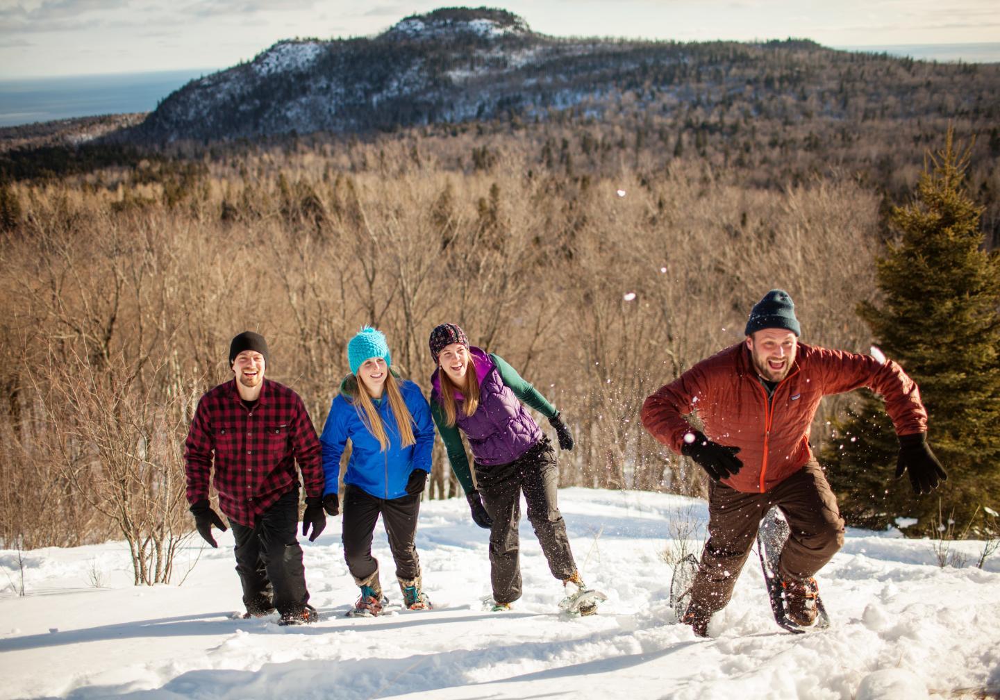 Group hiking uphill in snow, with mountain and forest in the background.