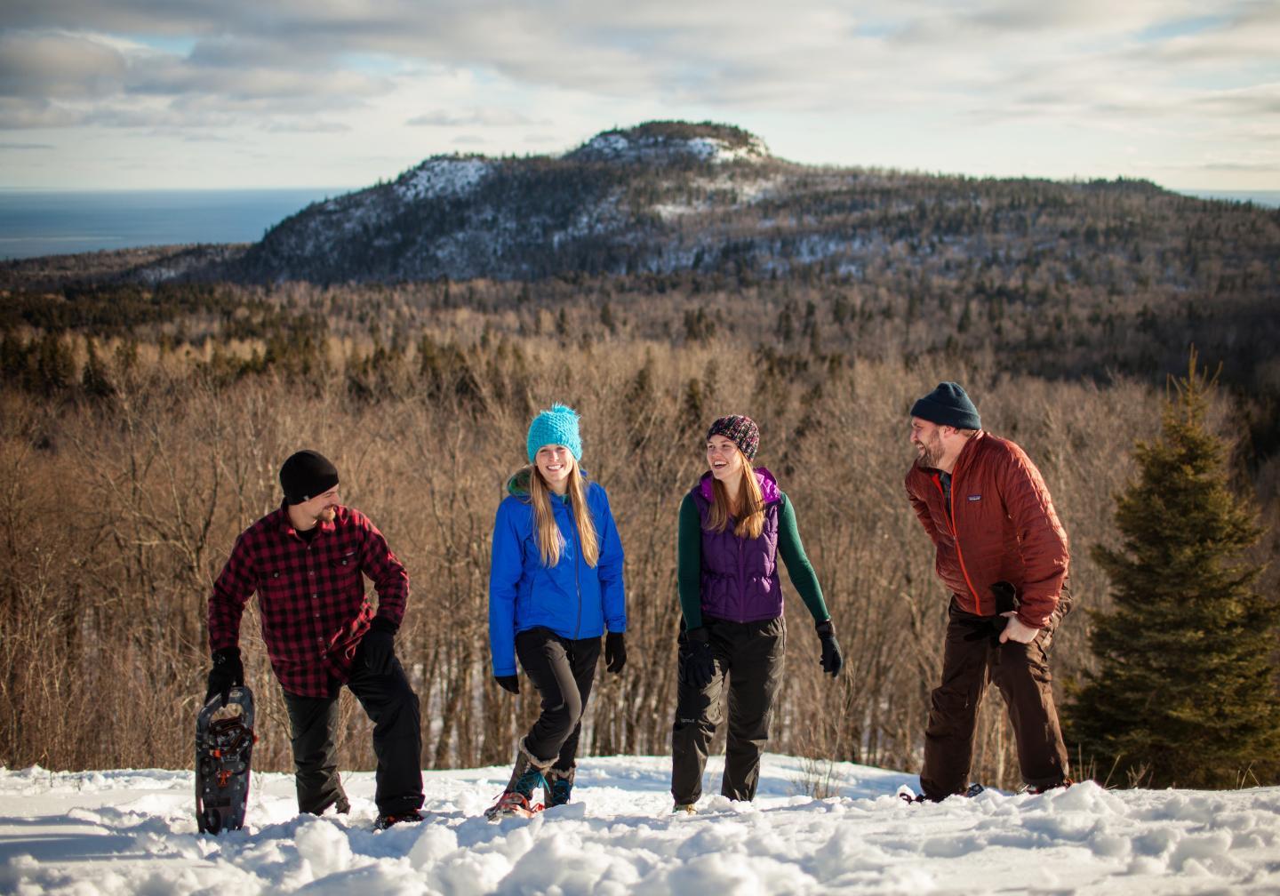 Four people standing on a snowy hill with a forested mountain in the background.