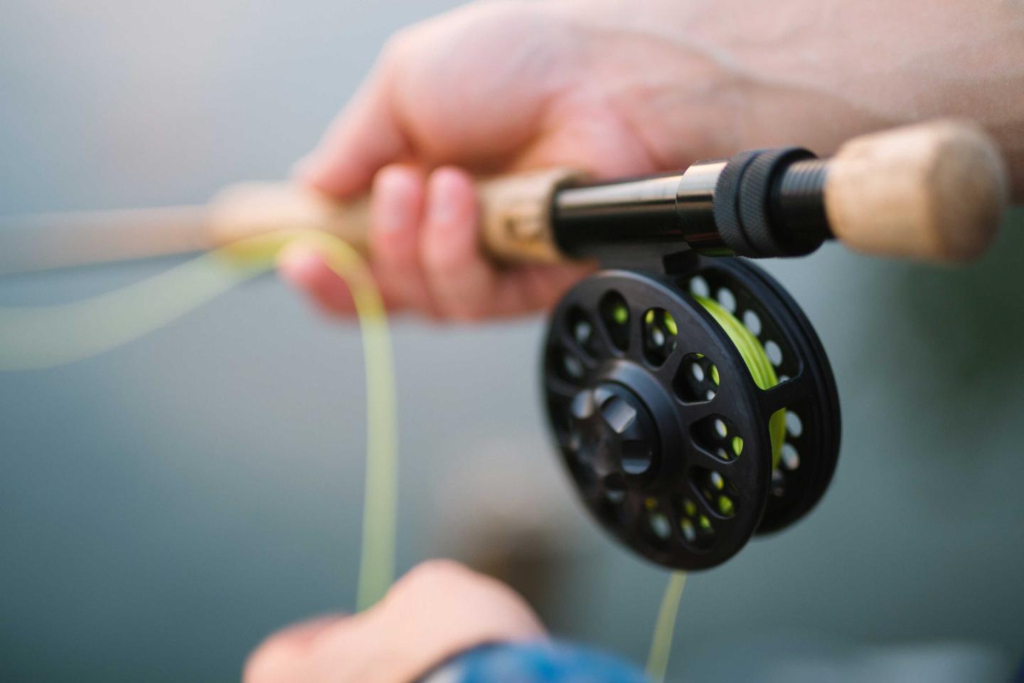 Hands holding a fishing rod with a fly reel.