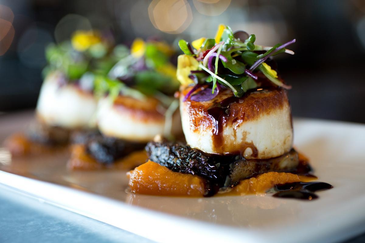 Seared scallops on puree with greens and sauce on a white plate.