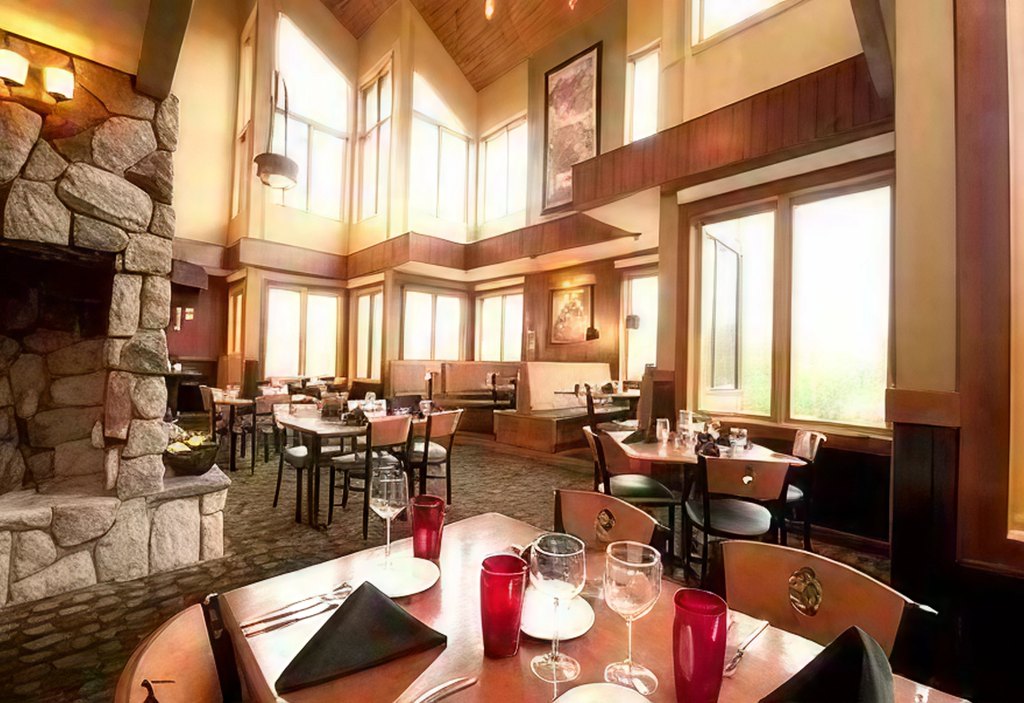 Cozy restaurant interior with large windows, wooden beams, and set tables.