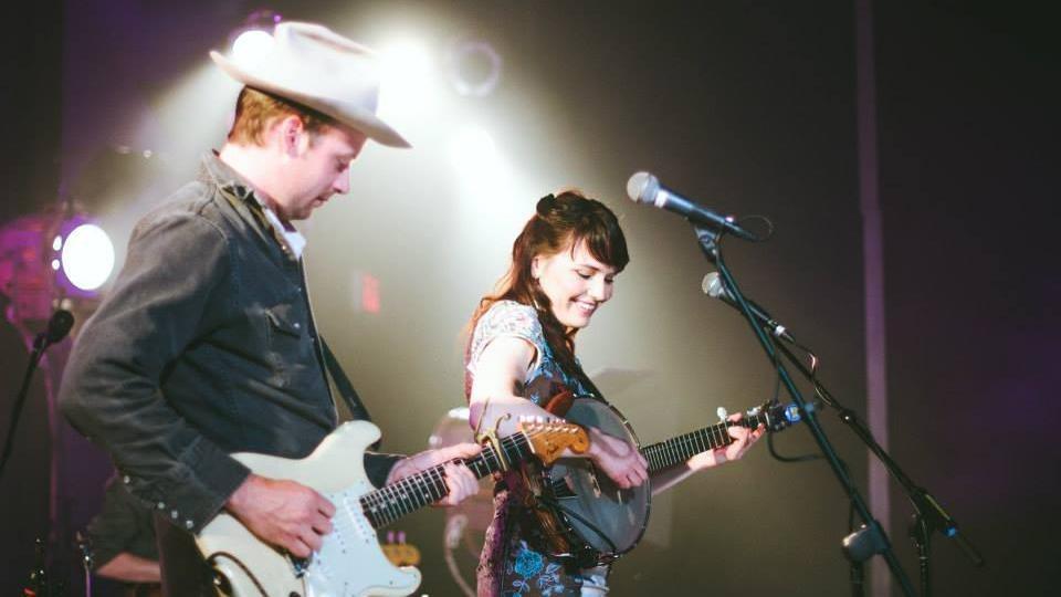 Musicians on stage with guitars under colorful lights.