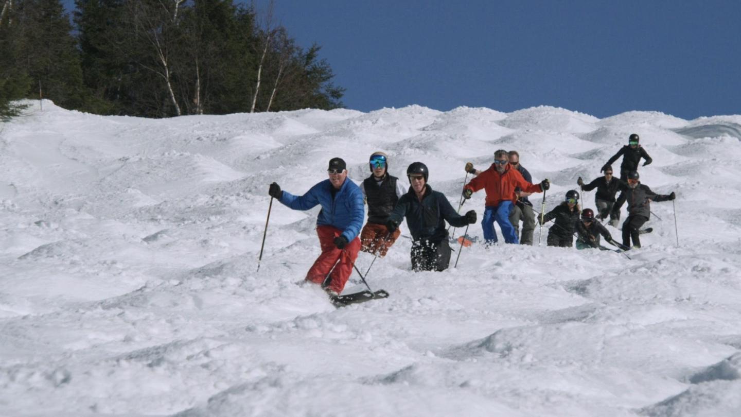 Skiers navigating snowy moguls under a clear blue sky.