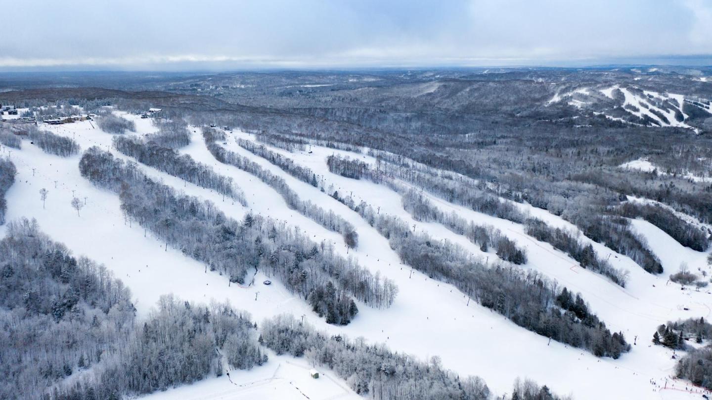 Snowy ski slopes on a forested hillside under a cloudy sky.