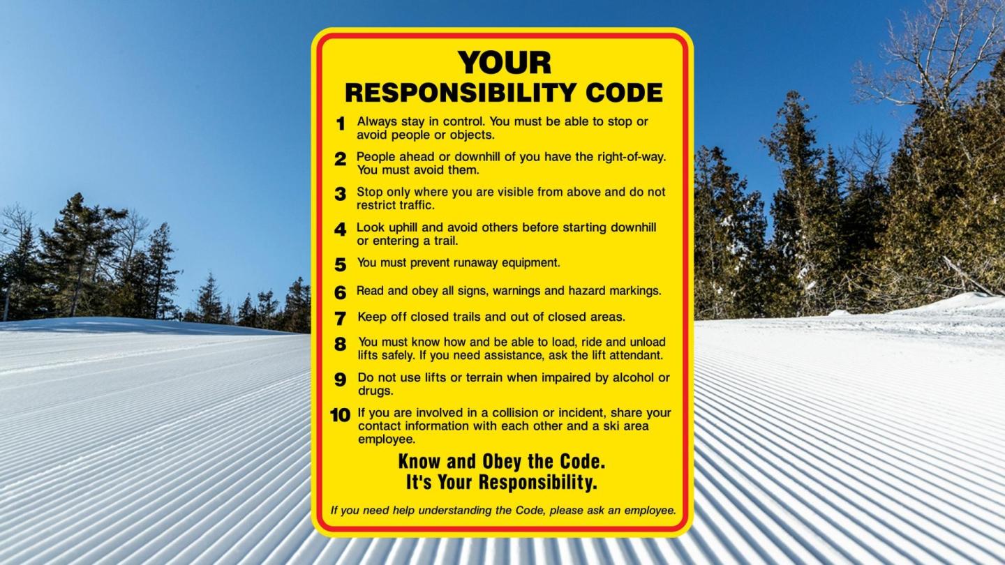 Yellow safety sign on a groomed snowy slope with trees in the background.