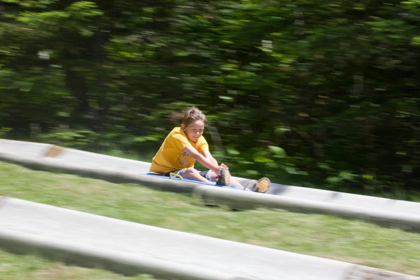 Child in yellow shirt sliding down a concrete track outdoors.