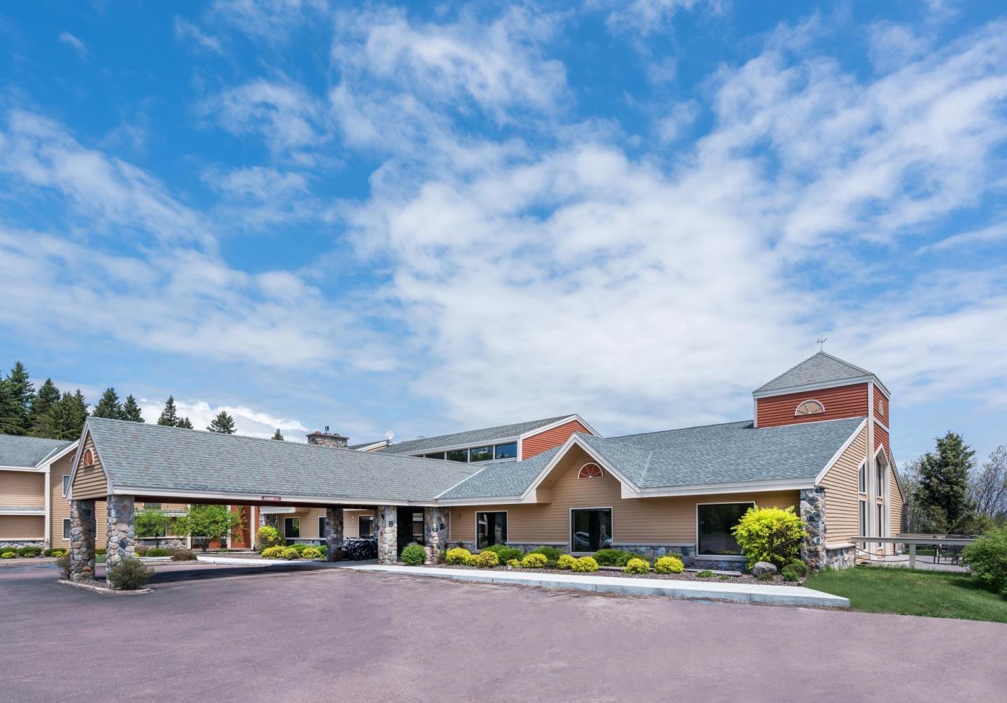 Hotel exterior with a covered entrance, blue sky, and landscaped greenery.