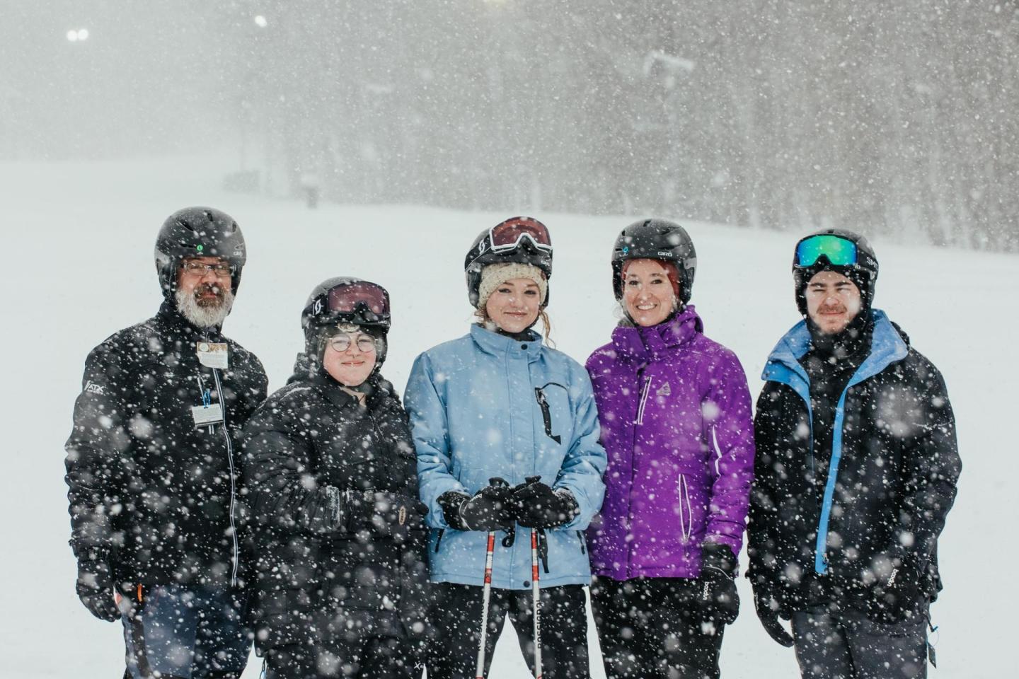 Five people in ski gear standing in the snow, smiling.