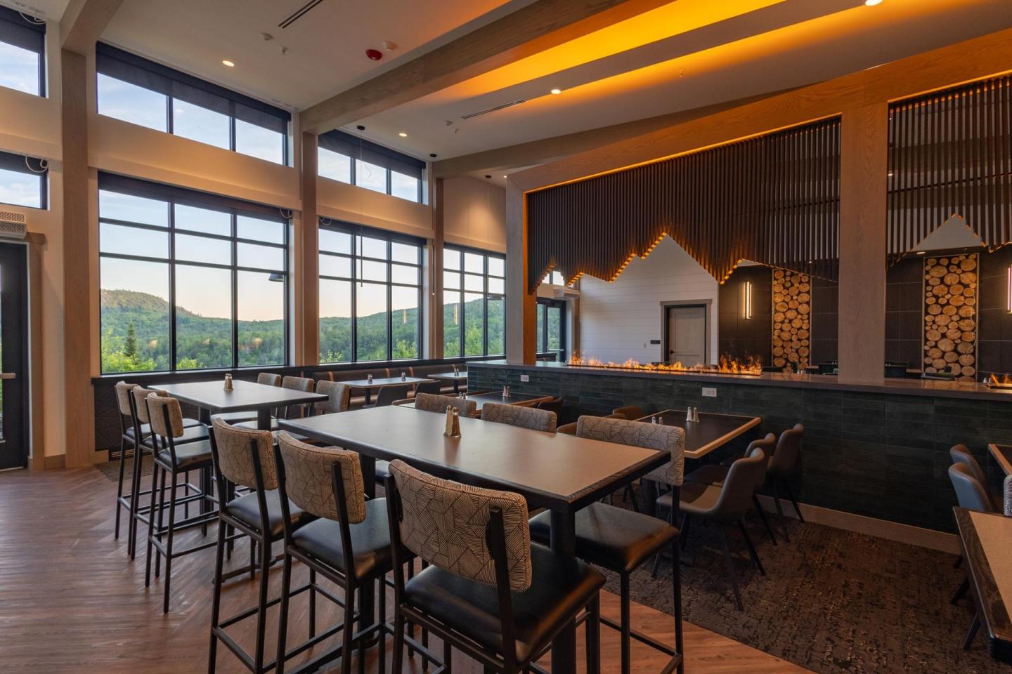 Spacious restaurant with large windows and modern decor, overlooking green hills.
