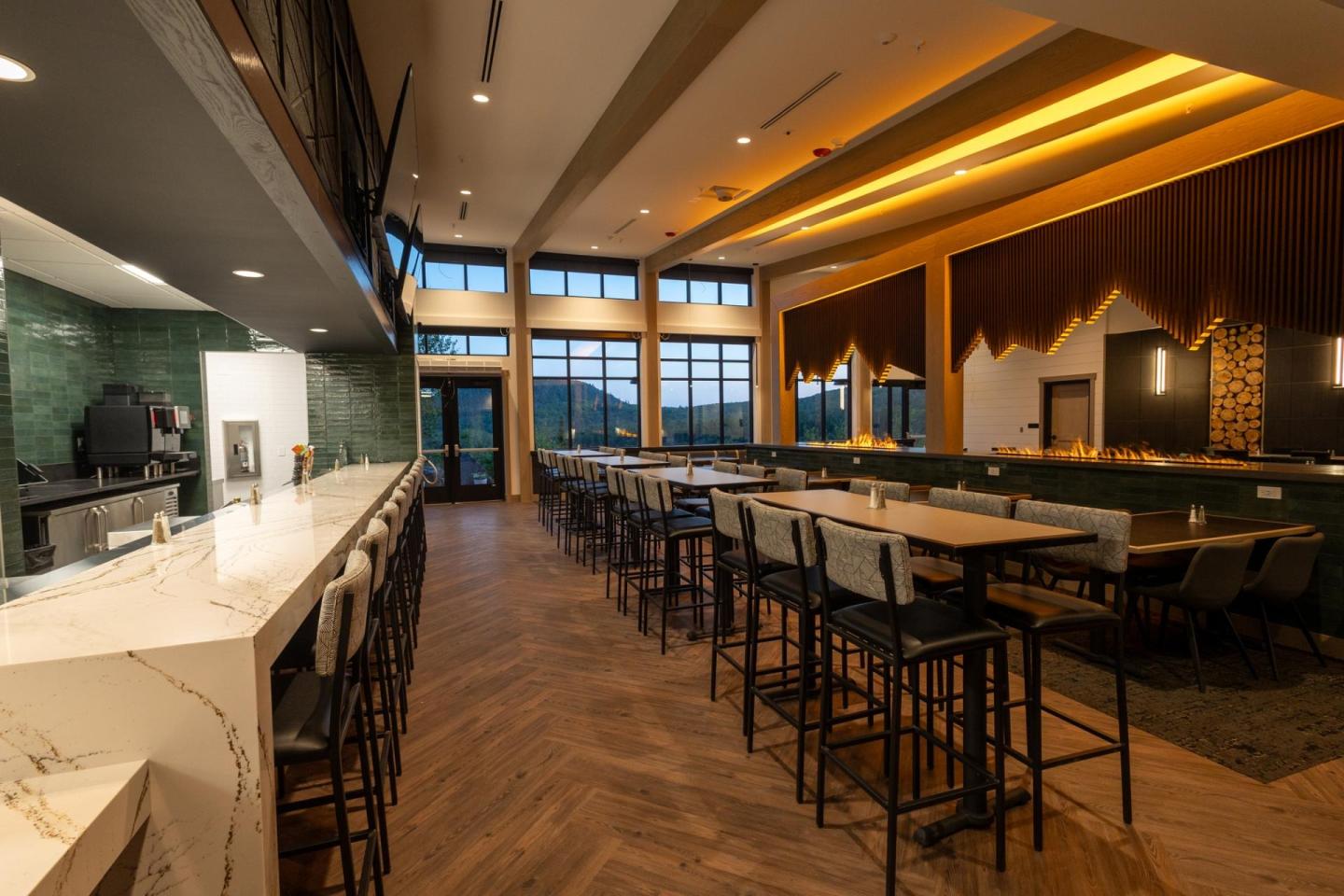 Modern restaurant interior with high tables, chairs, and warm lighting.