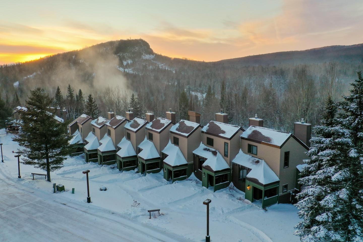 Row of snow-covered houses with a sunrise over forested hills.
