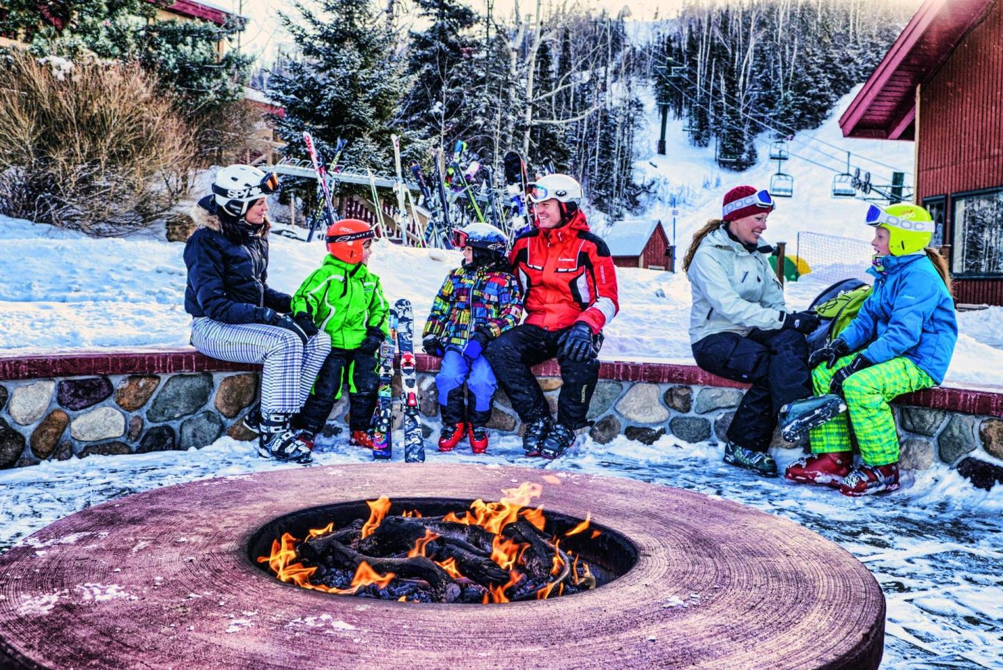 Group of people in winter gear sitting around an outdoor fire pit.