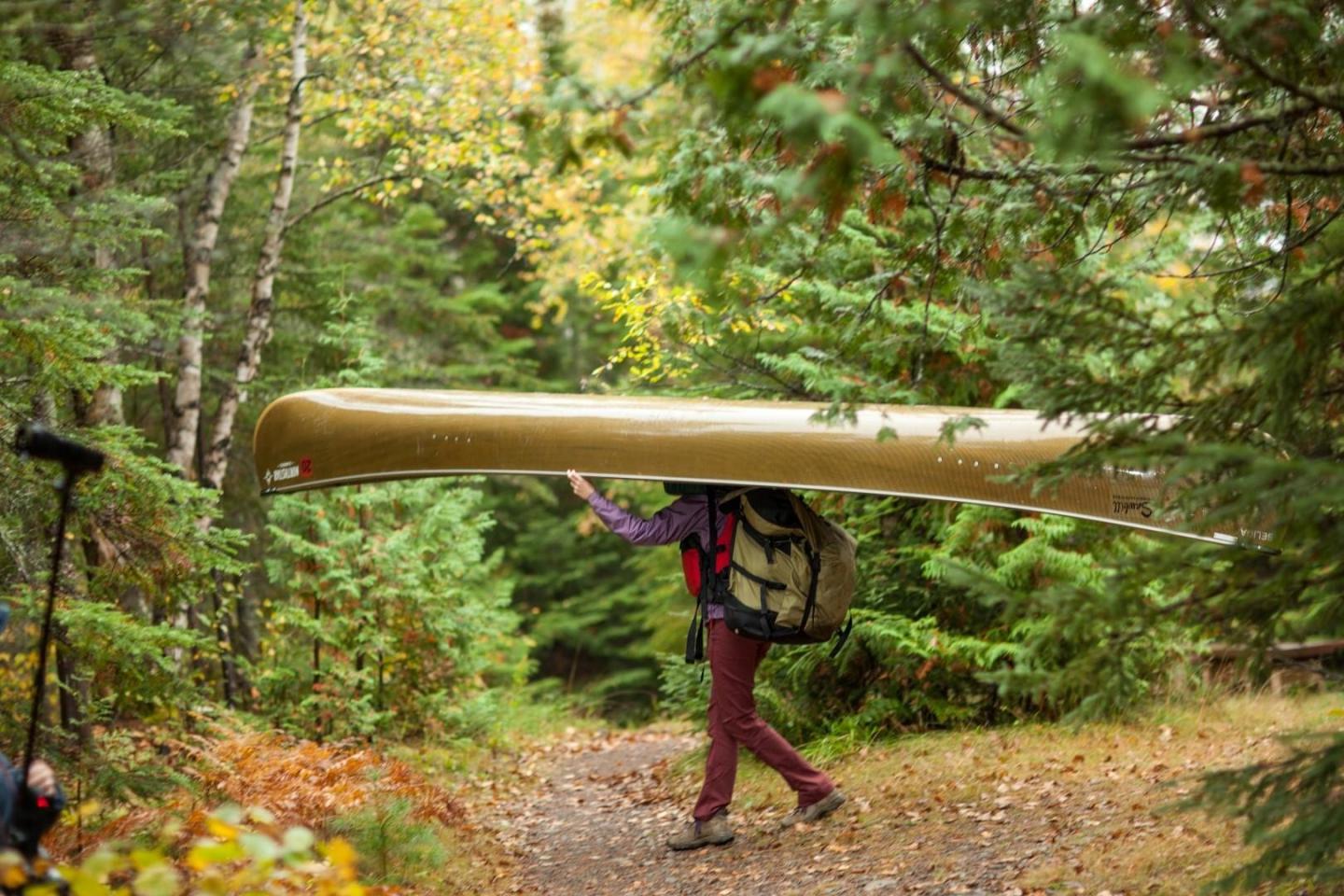 Person carrying canoe through forest trail.