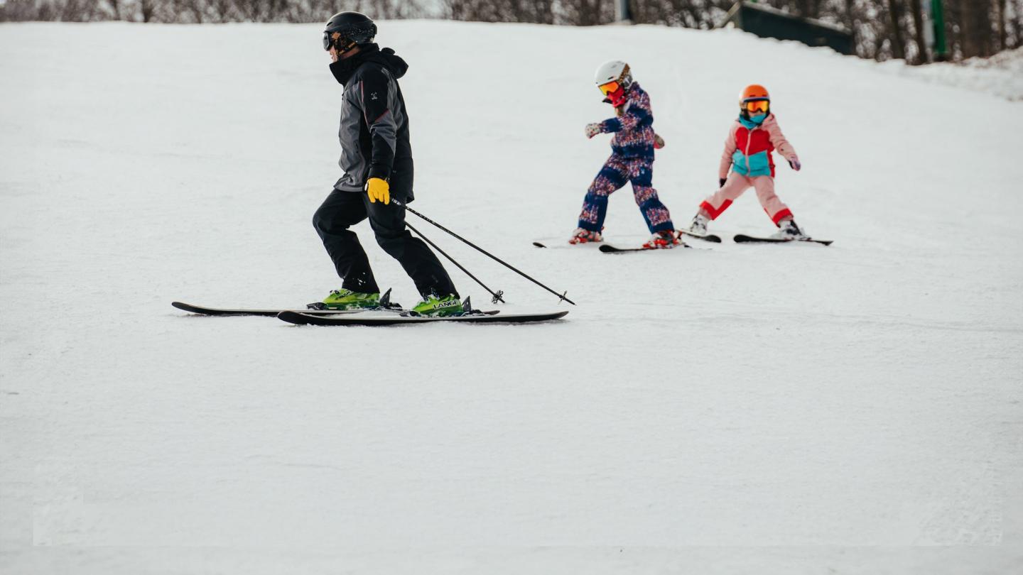 Ski instructor leading two children on a snowy slope.