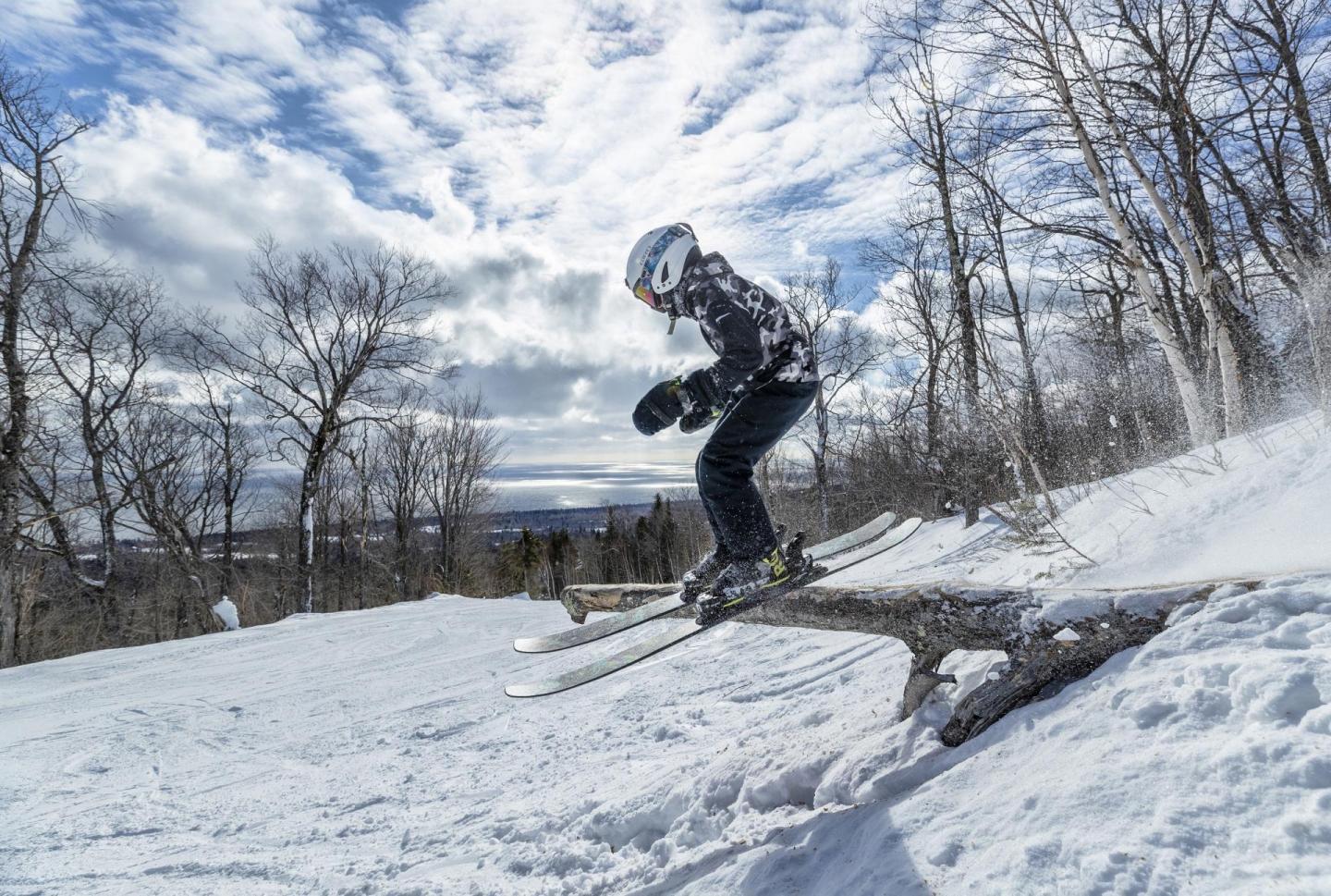 Skier jumping over a snow-covered log on a cloudy day.