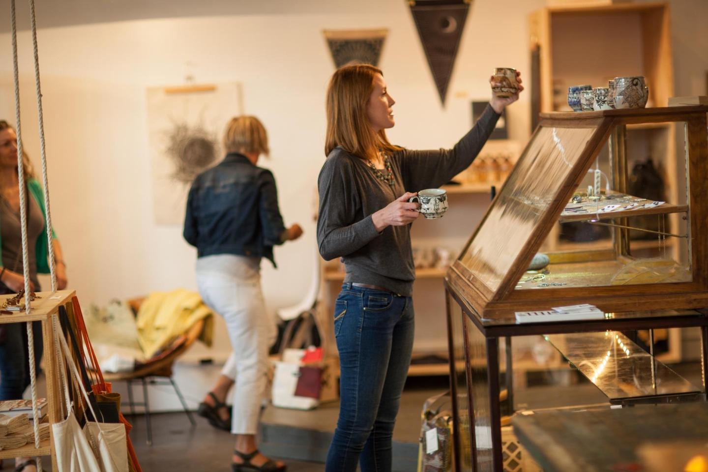 Woman shopping in an art gallery, holding a mug, examining items on display.