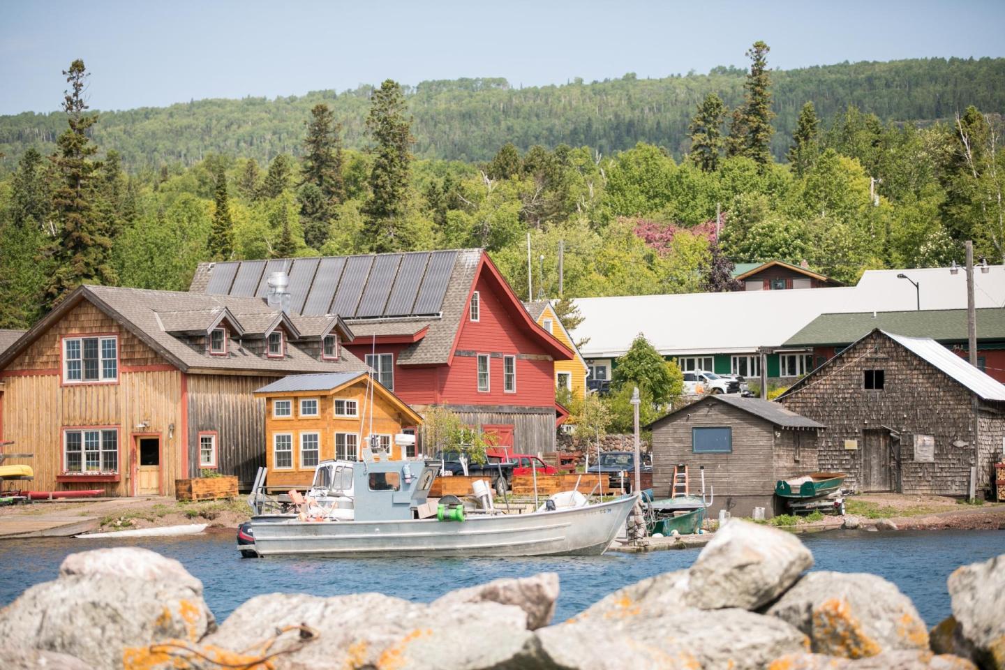 Rustic lakeside cabins with boats, set against a green forest under a clear sky.