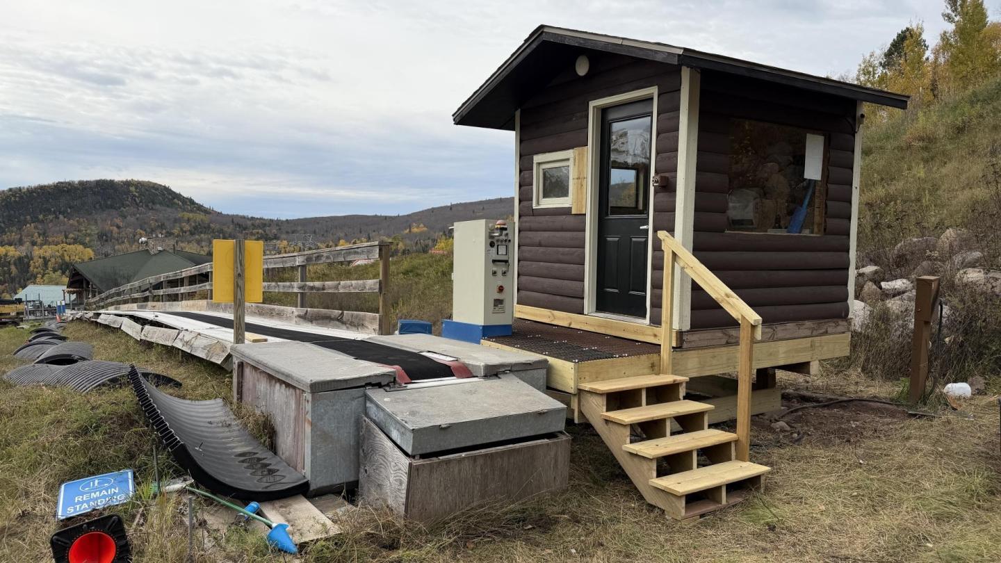 Small wooden cabin near a luge track with autumn foliage in the background.