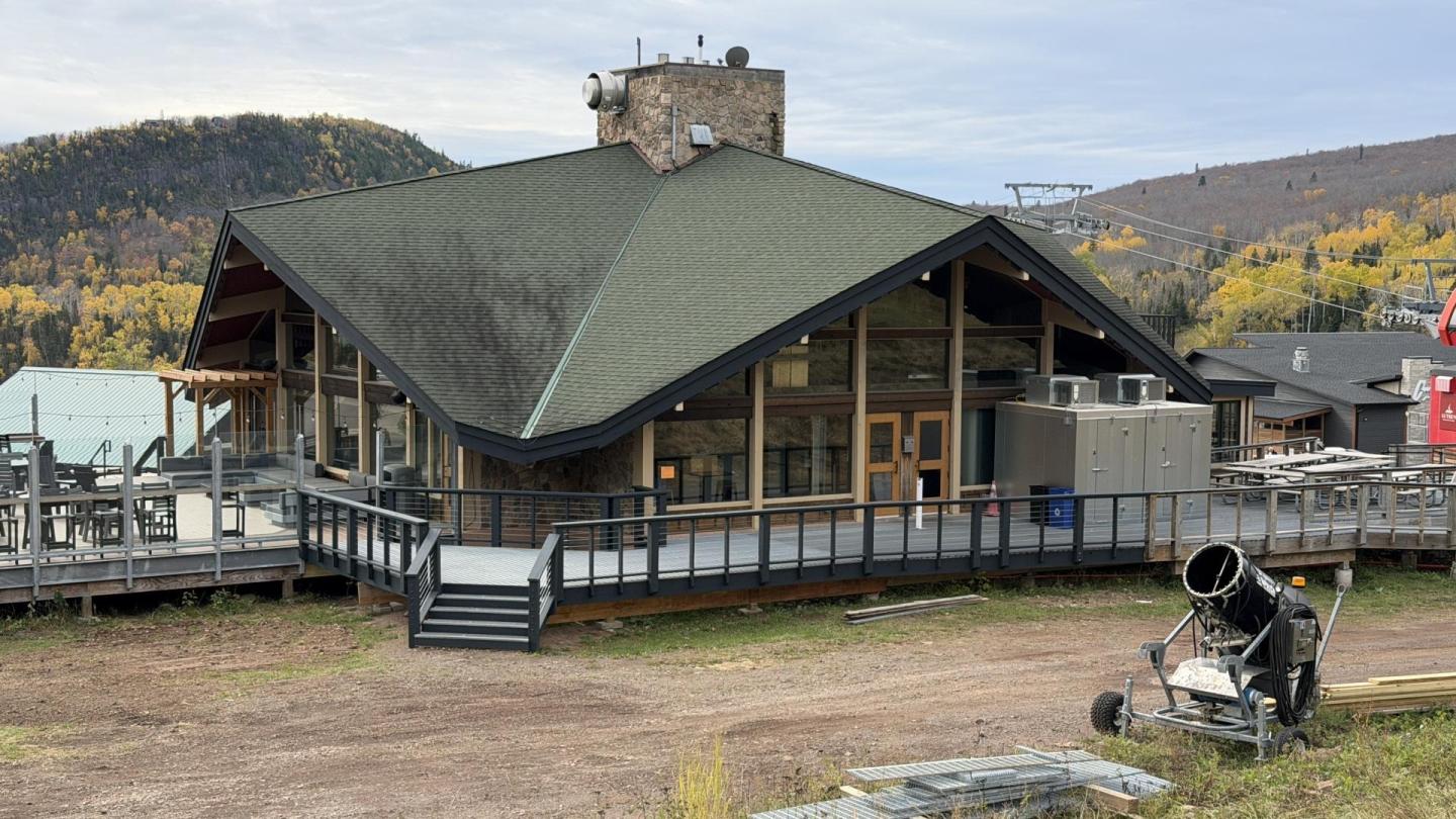 Rustic lodge with green roof in mountainous setting, autumn trees in background.