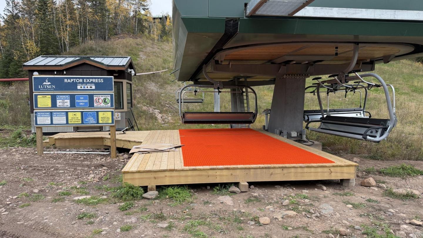 Ski lift with an orange mat and information board in a grassy setting.