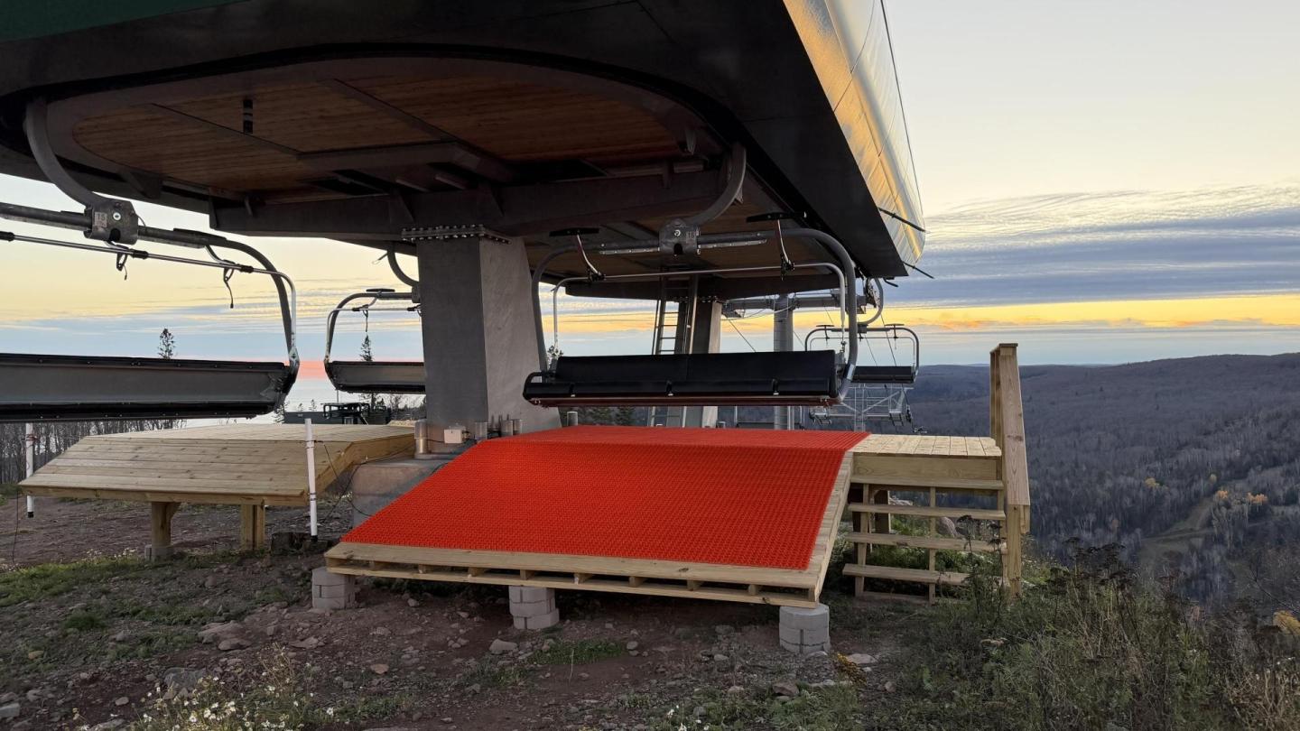 Ski lift with red mat at sunset, overlooking a forested valley.
